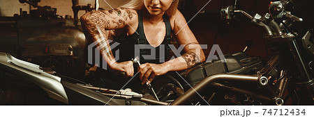 Blond woman mechanic repairing a motorcycle 74712434
