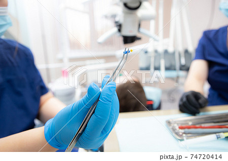 the dentist holds in his hand tweezers with a tool for the treatment of dental canals the dentist holds in his hand tweezers with a tool for the treatment of dental canals 74720414