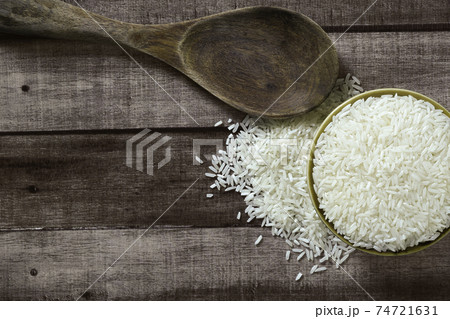 Uncooked dry Thai jasmine rice are overflow from bowl and wooden ladle beside put on wood floor, angle of view flat lay and top down horizontal view. Uncooked dry Thai jasmine rice are overflow from bowl and wooden ladle beside put on wood floor, angle of view flat lay and top down horizontal view. 74721631
