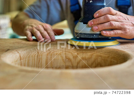 Woodworker sanding wooden furniture element in workshop 74722398