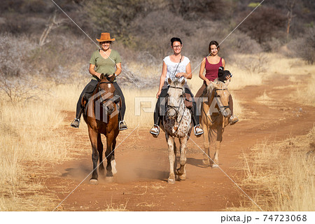 Three women ride horses on dirt track 74723068
