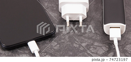 Black smartphone with connected plug of external powerbank. Mobile phone charging Black smartphone with connected plug of external powerbank. Mobile phone charging 74723197