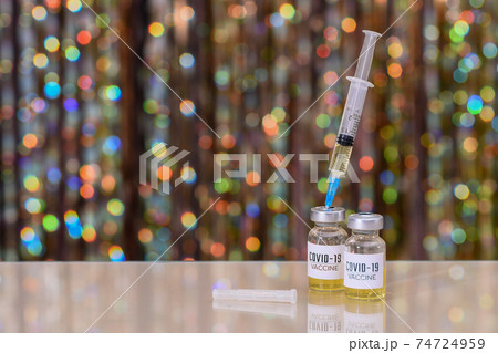 A bottle of of coronavirus vaccine. The syringe is inserted into a bottle with the covid-19 vaccine. On a shiny bokeh background.  74724959