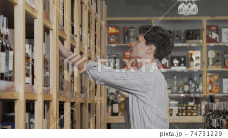 Young male winemaker organizing bottles on sale on the shelves at his store Young male winemaker organizing bottles on sale on the shelves at his store 74731229