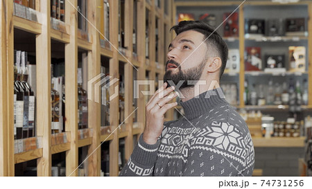 Handsome bearded man looking at the shelves with bottles at wine store Handsome bearded man looking at the shelves with bottles at wine store 74731256