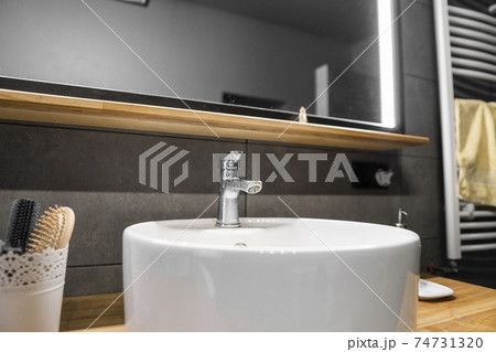 Bathroom interior with grey tile on a wall, stylish round sink and tap on a oak wood worktop. Minimalism in interior of bathroom. 74731320