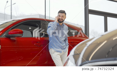 Charming man talking on his smart phone while choosing new car at the dealership Charming man talking on his smart phone while choosing new car at the dealership 74732324