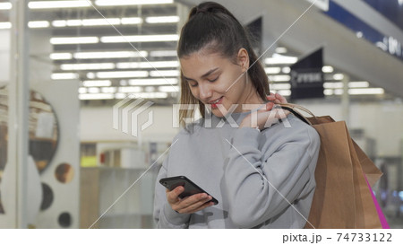 Lovely young woman using her smart phone while shopping at the mall Lovely young woman using her smart phone while shopping at the mall 74733122