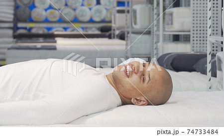 Happy African man lying on orthopedic mattress at furniture store 74733484