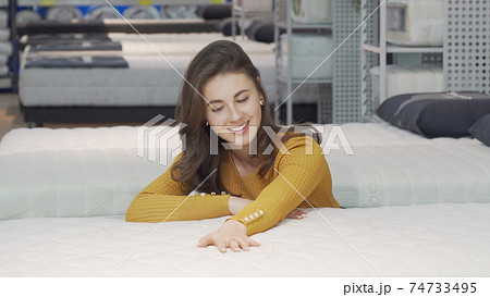 Beautiful happy woman examining orthopedic mattress on sale 74733495