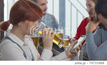 Young woman using her smart phone while drinking beer at the pub Young woman using her smart phone while drinking beer at the pub 74733966