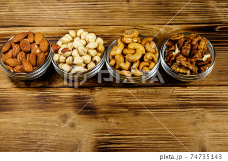 Assortment of nuts on wooden table. Almond, hazelnut, walnut and cashew in glass bowls. Healthy eating concept 74735143