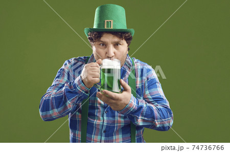Young Irish man in leprechaun party hat drinking green beer on Saint Patrick's Day Young Irish man in leprechaun party hat drinking green beer on Saint Patrick's Day 74736766