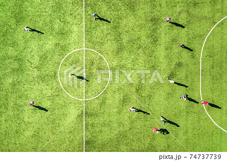 Top down aerial view of green football sports field and players playing football. Drone taken image of small unrecognizable sportsmen on grass covered stadium during sport activities. Top down aerial view of green football sports field and players playing football. Drone taken image of small unrecognizable sportsmen on grass covered stadium during sport activities. 74737739