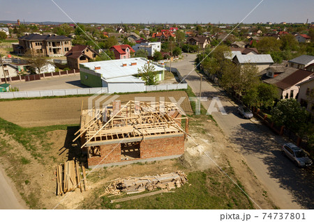 Aerial view of unfinished brick house with wooden roof frame structure under construction. 74737801
