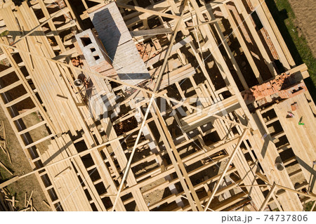Aerial view of unfinished brick house with wooden roof frame structure under construction. Aerial view of unfinished brick house with wooden roof frame structure under construction. 74737806