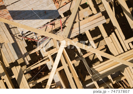 Aerial view of unfinished brick house with wooden roof frame structure under construction. 74737807