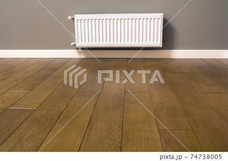White metal heating radiator mounted on gray wall inside a room. 74738005