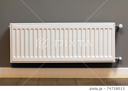 White metal heating radiator mounted on gray wall inside a room. White metal heating radiator mounted on gray wall inside a room. 74738013