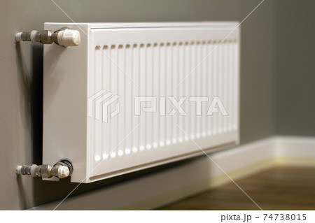 White metal heating radiator mounted on gray wall inside a room. White metal heating radiator mounted on gray wall inside a room. 74738015