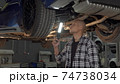 Handsome man examining lifted car with a lamp at the workshop 74738034