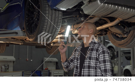 Handsome man examining lifted car with a lamp at the workshop Handsome man examining lifted car with a lamp at the workshop 74738034
