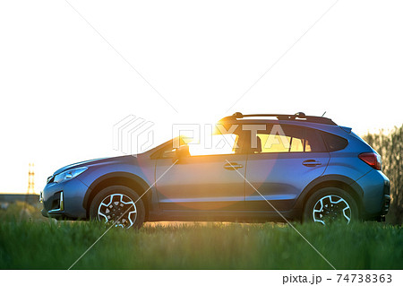 Landscape with blue off road car on green grass at sunset. Traveling by auto, adventure in wildlife, expedition or extreme travel on a SUV automobile. Offroad 4x4 vehicle in field at sunrise. 74738363