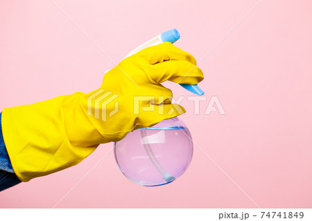A hand in a yellow glove holds a spray of cleaning fluid on a pink background. A hand in a yellow glove holds a spray of cleaning fluid on a pink background. 74741849