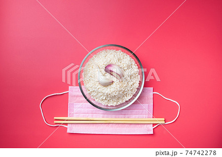 Bowl with rice, garlic and chopsticks on a pink background and a medical mask.  74742278