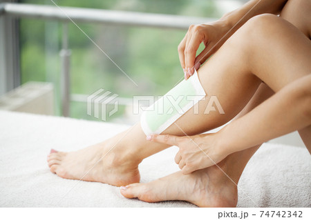 Woman uses wax tape to remove hair on legs 74742342