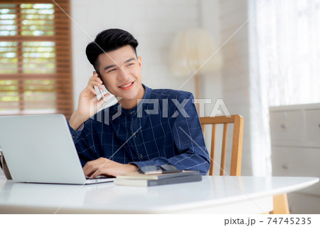 Young asian man talking phone and work from home with laptop computer, freelance using notebook. 74745235