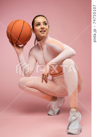 Joyful young woman with basketball ball crouching down in studio Joyful young woman with basketball ball crouching down in studio 74750107