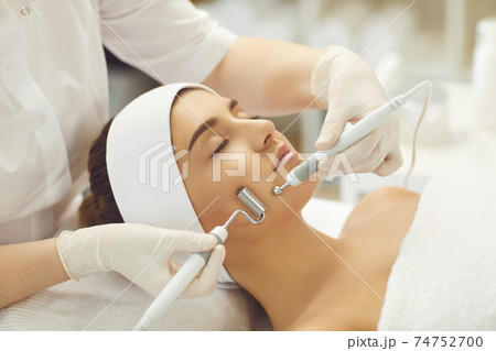 Woman face receiving facial microcurrent treatment with apparatus from therapist 74752700