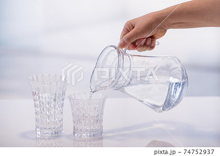 Hand pouring water from a jar into a glass 74752937
