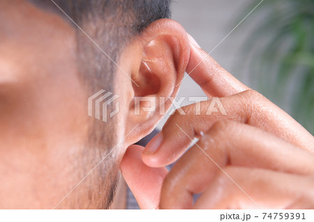 close up of young man holding ear suffering pain  74759391