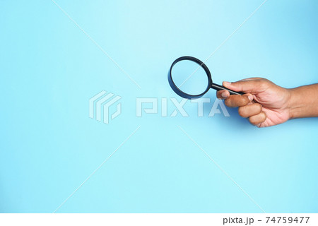 hand holding magnifying glass on blue with copy space  74759477
