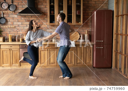 Overjoyed man and woman holding hands, dancing in modern kitchen 74759960