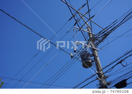 青空の下 電信柱に周りの家から電線が集中して集まっている様子の写真素材