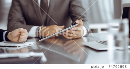 Unknown businessman using tablet computer and working together with his colleague while sits at the glass desk in modern office. Teamwork and partnership concept 74762698