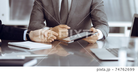 Unknown businessman using tablet computer and working together with his colleague while sits at the glass desk in modern office. Teamwork and partnership concept 74762699