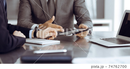 Unknown businessman using tablet computer and working together with his colleague while sits at the glass desk in modern office. Teamwork and partnership concept 74762700