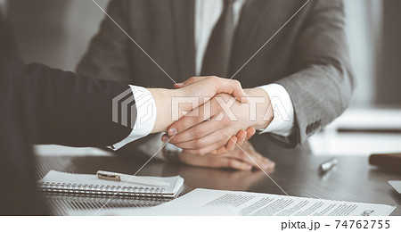 Unknown businessman shaking hands with his colleague or partner above the glass desk in modern office, close-up. Business people group at meeting 74762755