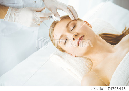 Beautician doctor doing beauty procedure with syringe to blonde female face. Cosmetic medicine, beauty injections concept 74763443