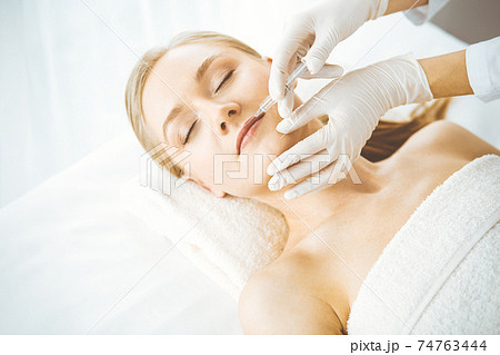 Beautician doctor doing beauty procedure with syringe to blonde female face. Cosmetic medicine, beauty injections concept 74763444