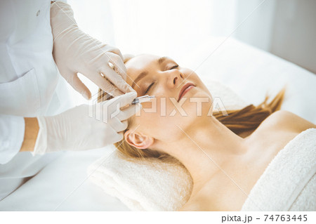 Beautician doctor doing beauty procedure with syringe to blonde female face. Cosmetic medicine, beauty injections concept 74763445