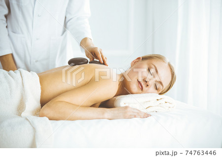 Beautiful happy woman enjoying warm stones procedure with closed eyes. Beauty and Spa salon concept 74763446
