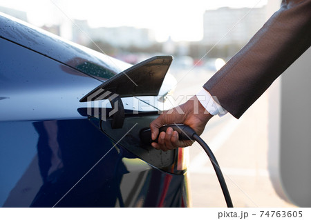 Close-up of man's hand, inserting a charger into his electric car against the background of blurred city buildings 74763605