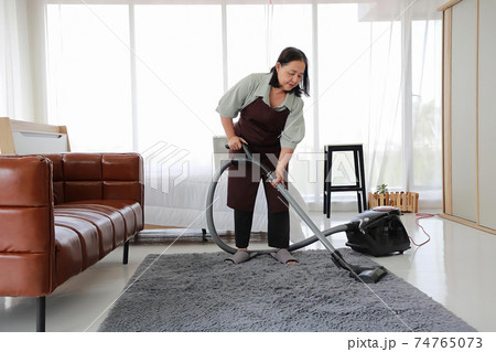 Senior woman cleaning the carpet with vacuum cleaner in the living room. Senior woman cleaning the carpet with vacuum cleaner in the living room. 74765073