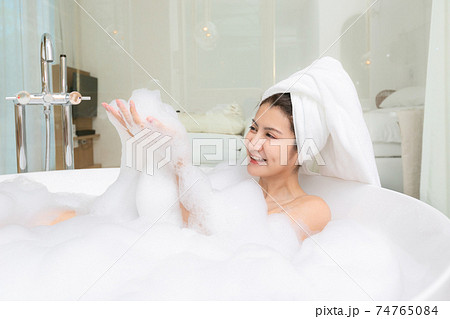 Happy asian woman bathes with white foam in a bathtub fun emotions. Happy asian woman bathes with white foam in a bathtub fun emotions. 74765084