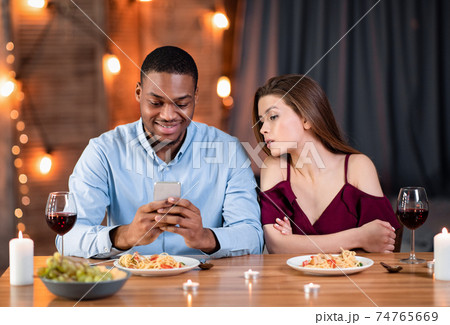 Jealous young woman peeking into boyfriend's smartphone, reading his messages during dinner 74765669